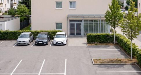 Hotelparkplatz am Mittag, nur wenige Stellplätze belegt, im Hintergrund das Hotelgebäude